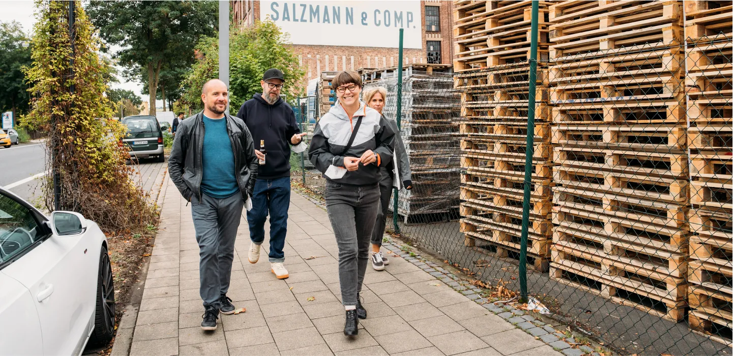 Four machbar.de team members walk past a street with stacked wooden pallets and a building displaying "SALZMANN & COMP.".