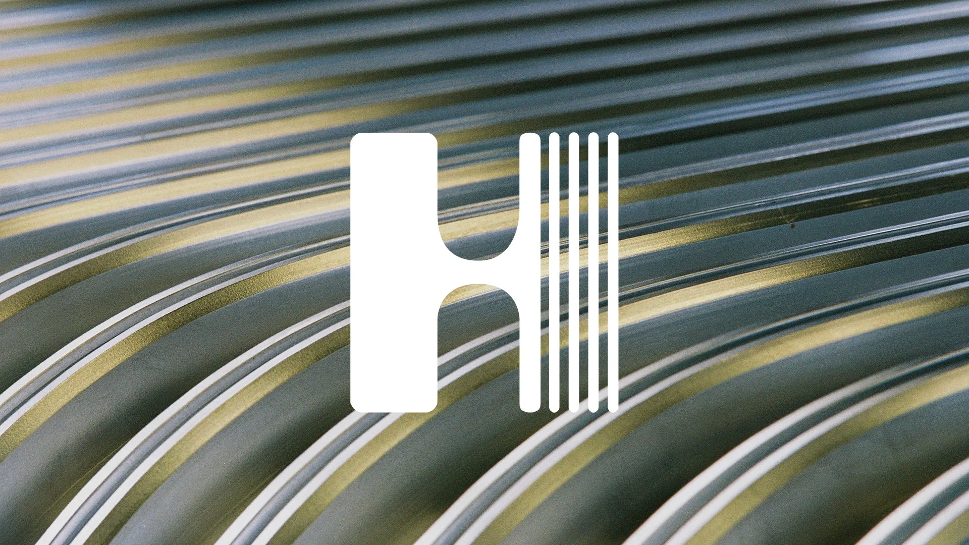 Das weiße Hübner-Logo auf einem Hintergrund Detailaufnahme eines Faltenbalgs, wie er in Bussen und Bahnen verwendet wird.