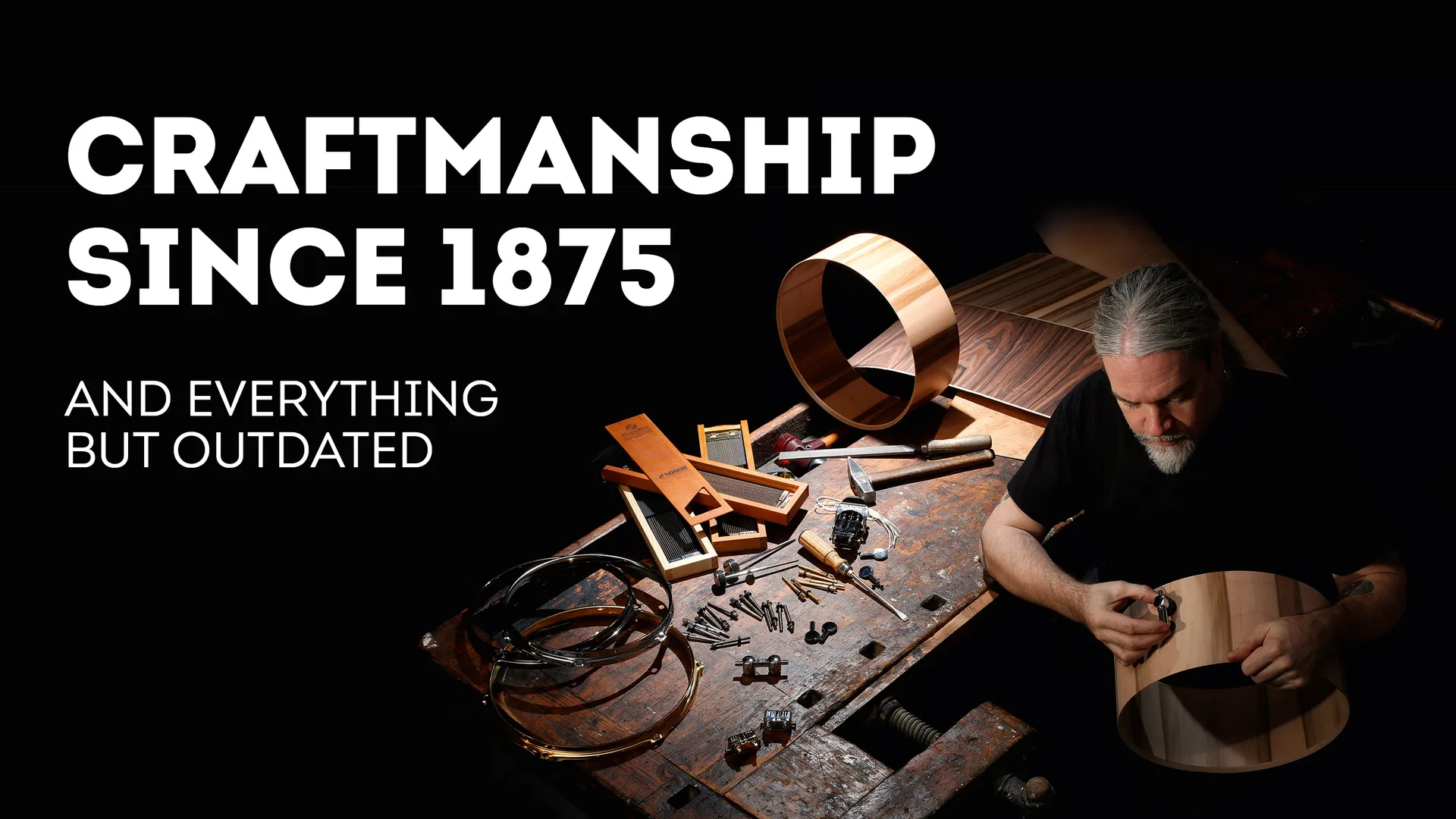 An older man at a dramatically lit workbench holds a fastening to a wooden drum, with the promotional headline 'Craftmanship since 1875'.