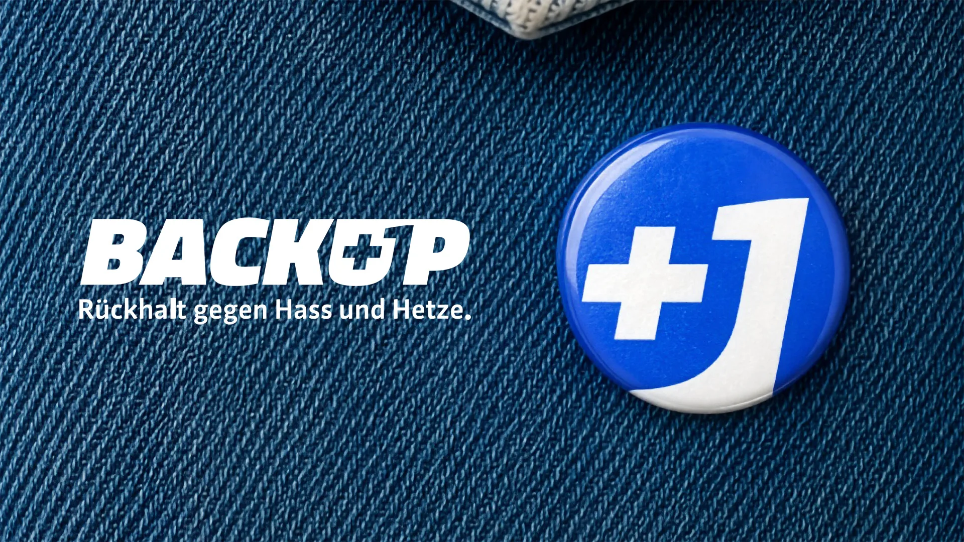 Logo &quot;BACKUP&quot; mit Claim &quot;Rückhalt gegen Hass und Hetze&quot; und Ansteck-Pin mit &quot;+1&quot; auf blauem Jeansstoff.